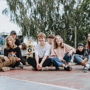 Happy group of teenage skateboarders sitting together outdoors having fun and posing for photos.