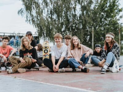 Happy group of teenage skateboarders sitting together outdoors having fun and posing for photos.