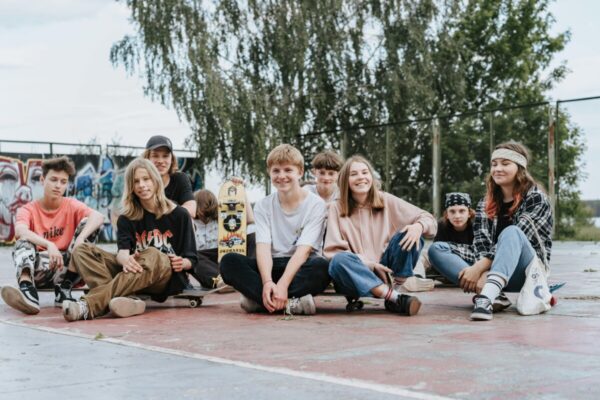 Happy group of teenage skateboarders sitting together outdoors having fun and posing for photos.